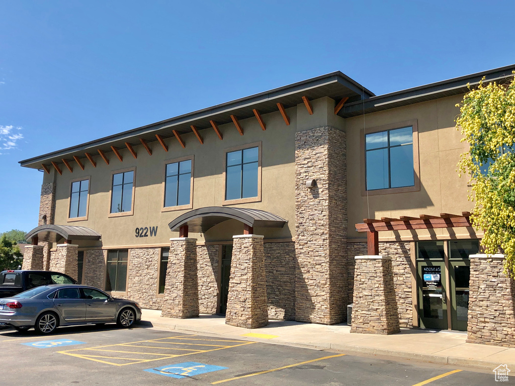 View of front facade with stone siding, uncovered parking, and stucco siding
