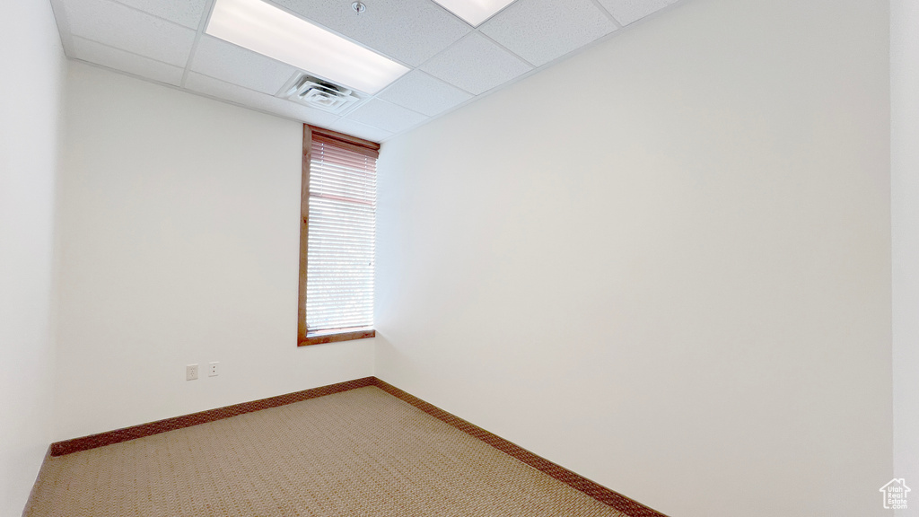 Empty room with a drop ceiling, baseboards, light colored carpet, and visible vents