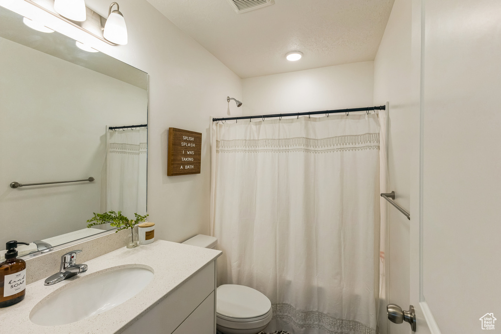 Full bath featuring a shower with shower curtain, toilet, and vanity
