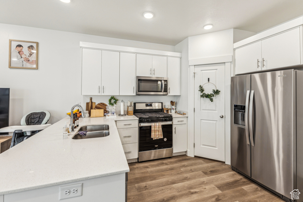 Kitchen featuring white cabinetry, stainless steel appliances, a sink, a peninsula, and wood finished floors