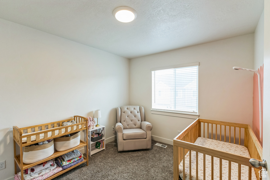 Carpeted bedroom featuring a crib, a textured ceiling, baseboards, and visible vents