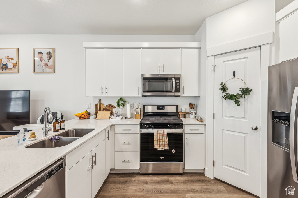 Kitchen featuring light countertops, a sink, white cabinetry, wood finished floors, and appliances with stainless steel finishes