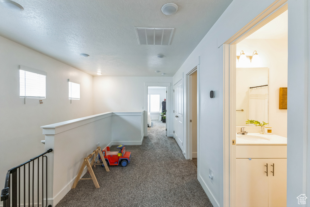 Hall featuring carpet flooring, a sink, a wealth of natural light, and visible vents