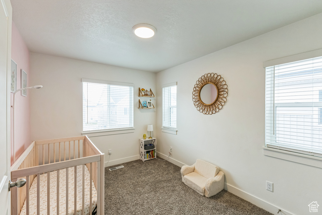 Bedroom with a nursery area, a textured ceiling, dark colored carpet, baseboards, and visible vents