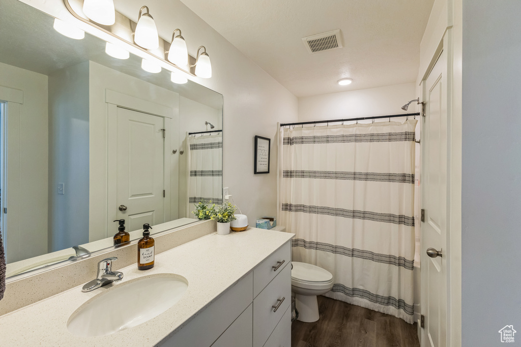Bathroom with toilet, curtained shower, vanity, wood finished floors, and visible vents