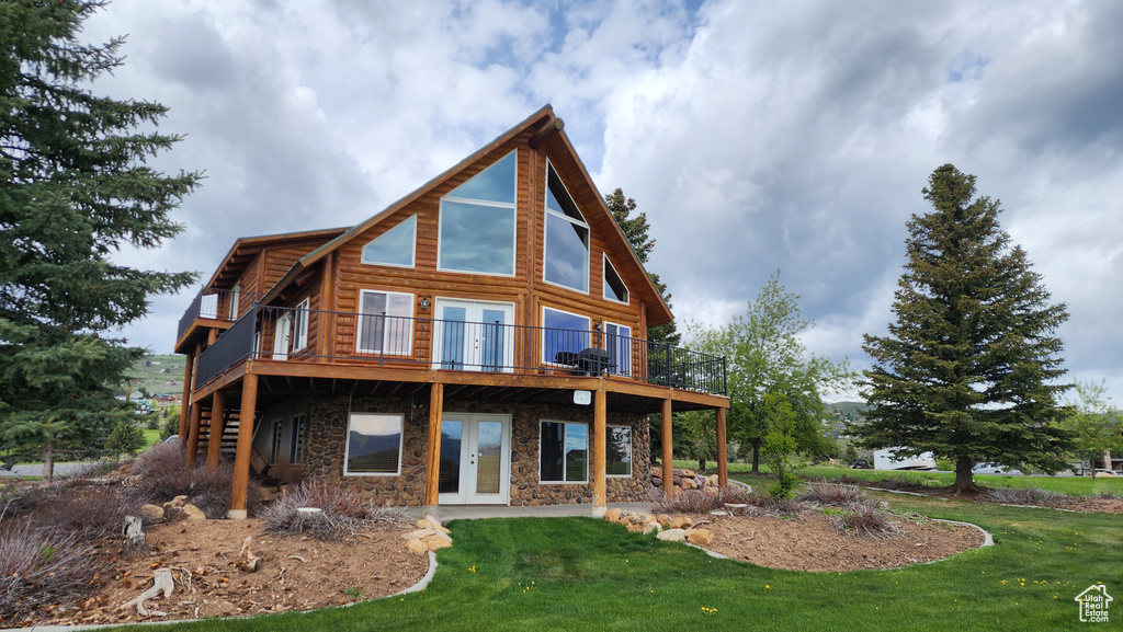 Rear view of property featuring french doors, stone siding, a wooden deck, and a yard