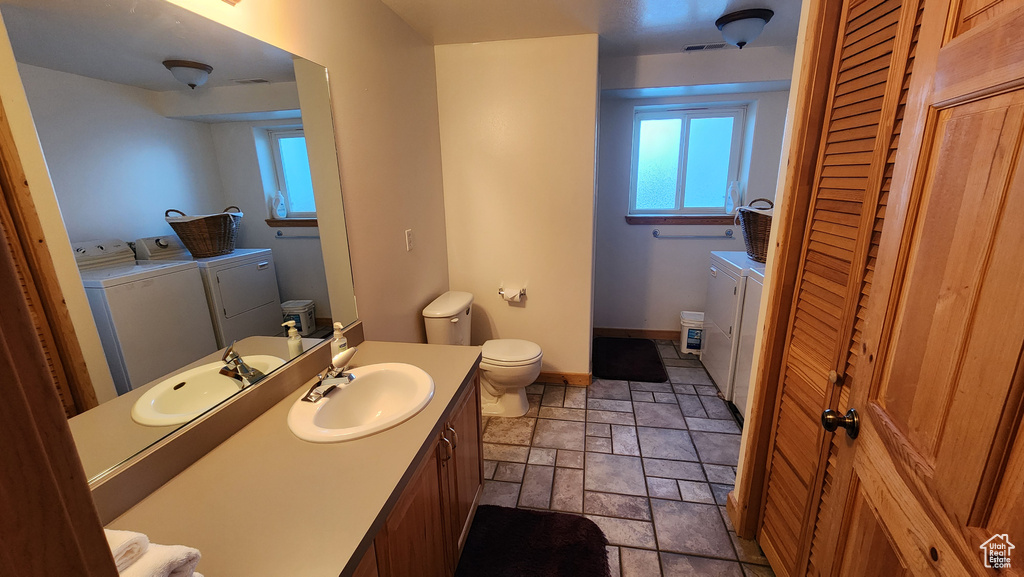 Bathroom featuring stone finish floor, toilet, washing machine and clothes dryer, and a wealth of natural light