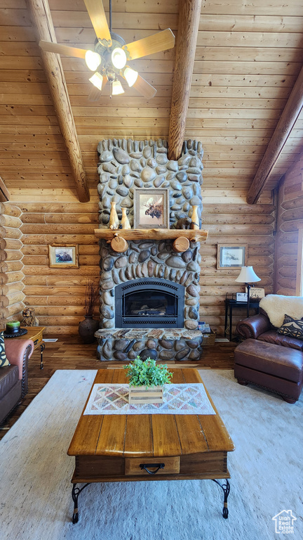 Living room with lofted ceiling with beams, wood ceiling, ceiling fan, a stone fireplace, and wood finished floors