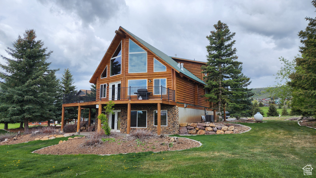 Rear view of house with stone siding, a yard, a deck, and log exterior