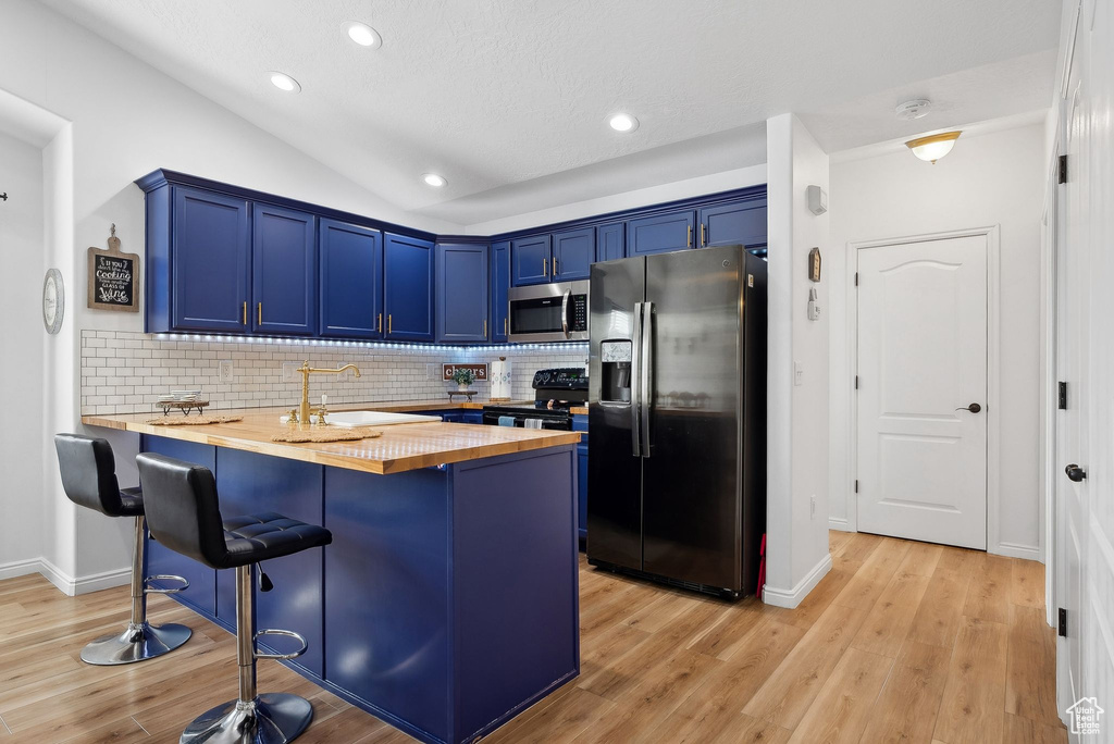 Kitchen featuring a kitchen breakfast bar, butcher block countertops, light wood-style flooring, stainless steel appliances, and blue cabinetry