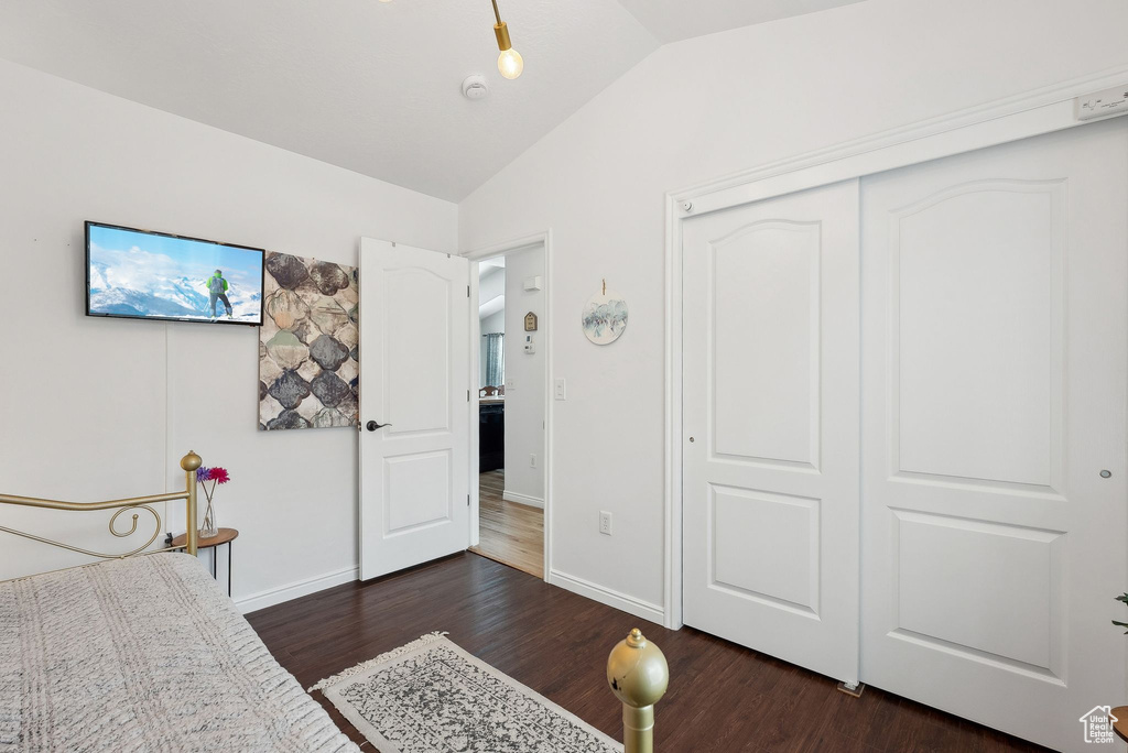 Bedroom featuring a closet, dark wood-type flooring, lofted ceiling, and baseboards