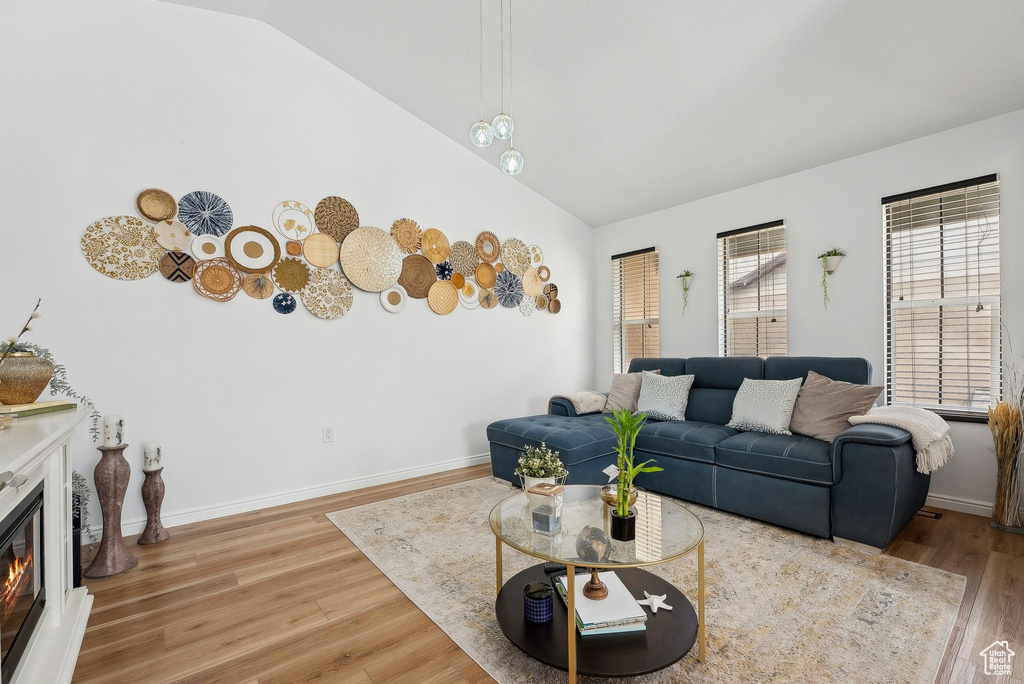 Living area featuring baseboards, lofted ceiling, a glass covered fireplace, and light wood-type flooring