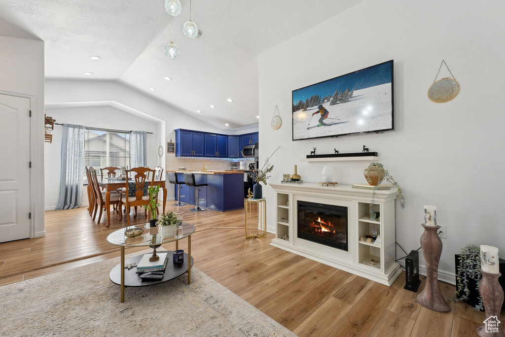 Living room with baseboards, vaulted ceiling, light wood-style flooring, and a glass covered fireplace
