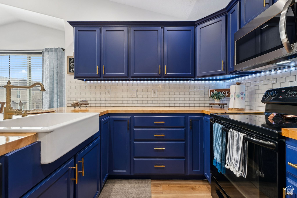 Kitchen with a sink, black / electric stove, blue cabinets, and stainless steel microwave
