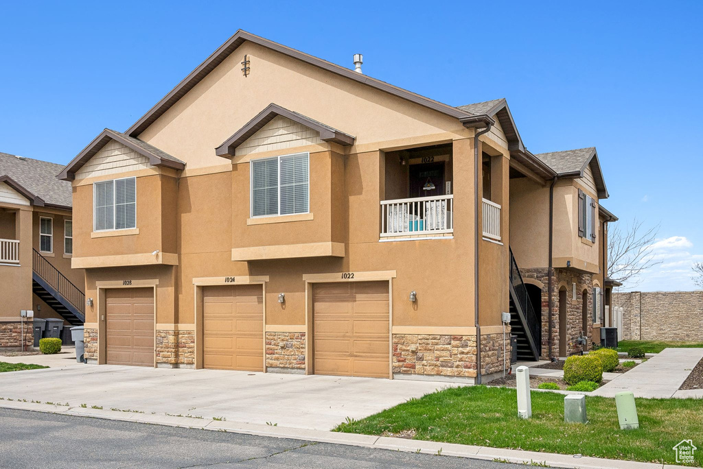 Townhome / multi-family property with driveway, stone siding, stairway, stucco siding, and an attached garage