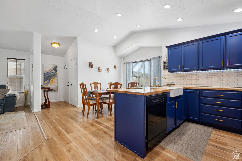 Kitchen featuring blue cabinetry, vaulted ceiling, a sink, wood counters, and black dishwasher