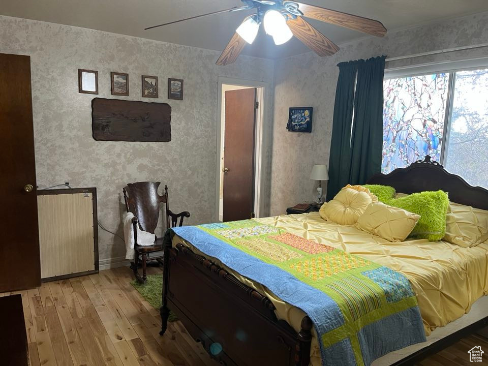Bedroom with ceiling fan, wallpapered walls, and light wood-style floors