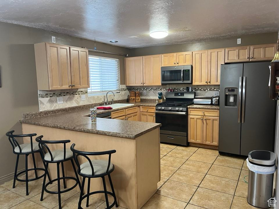 Kitchen with a sink, tasteful backsplash, a peninsula, light brown cabinets, and stainless steel appliances