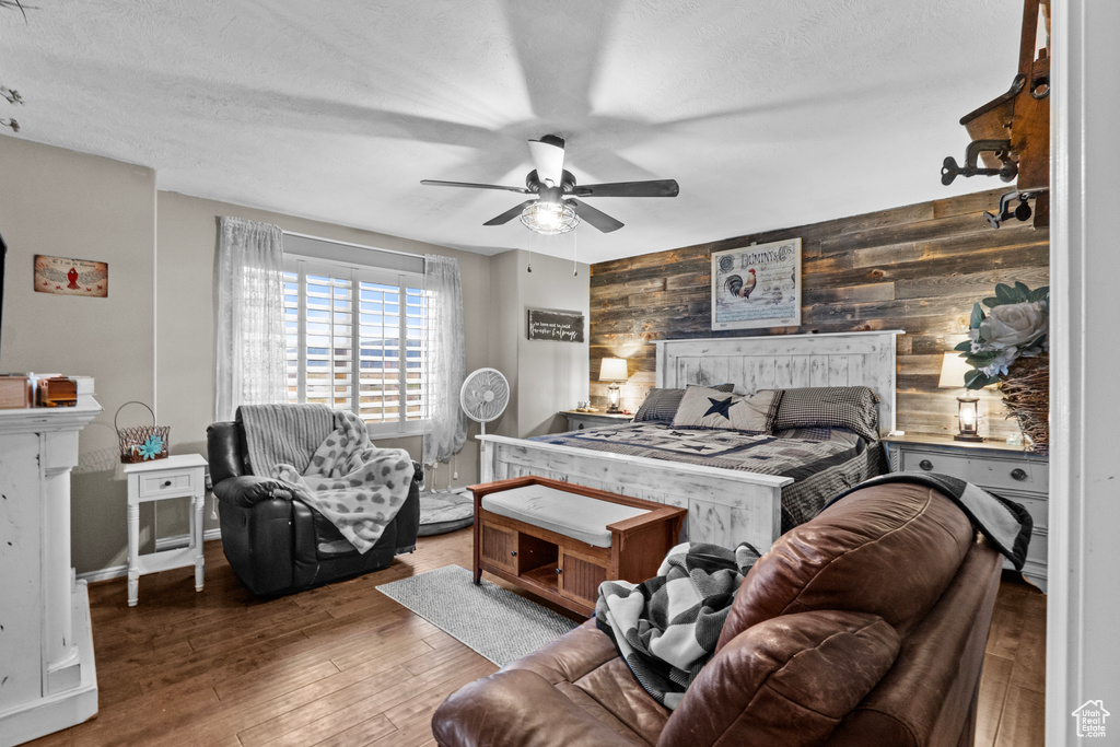 Bedroom featuring a textured ceiling, wooden walls, ceiling fan, and wood finished floors
