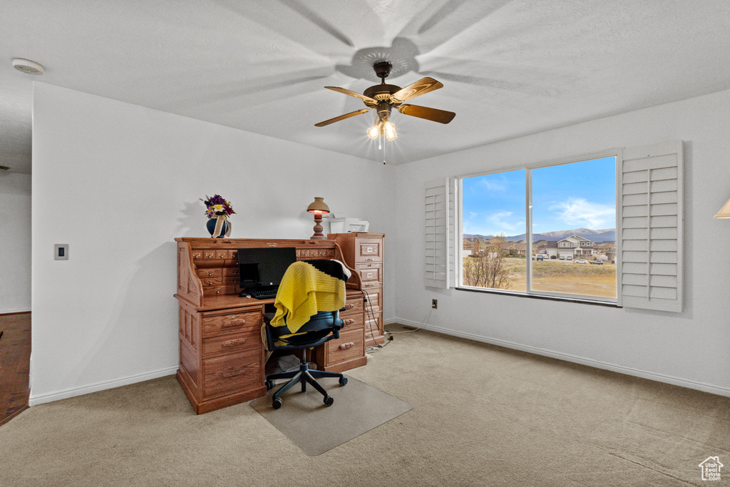 Carpeted home office featuring a ceiling fan and baseboards