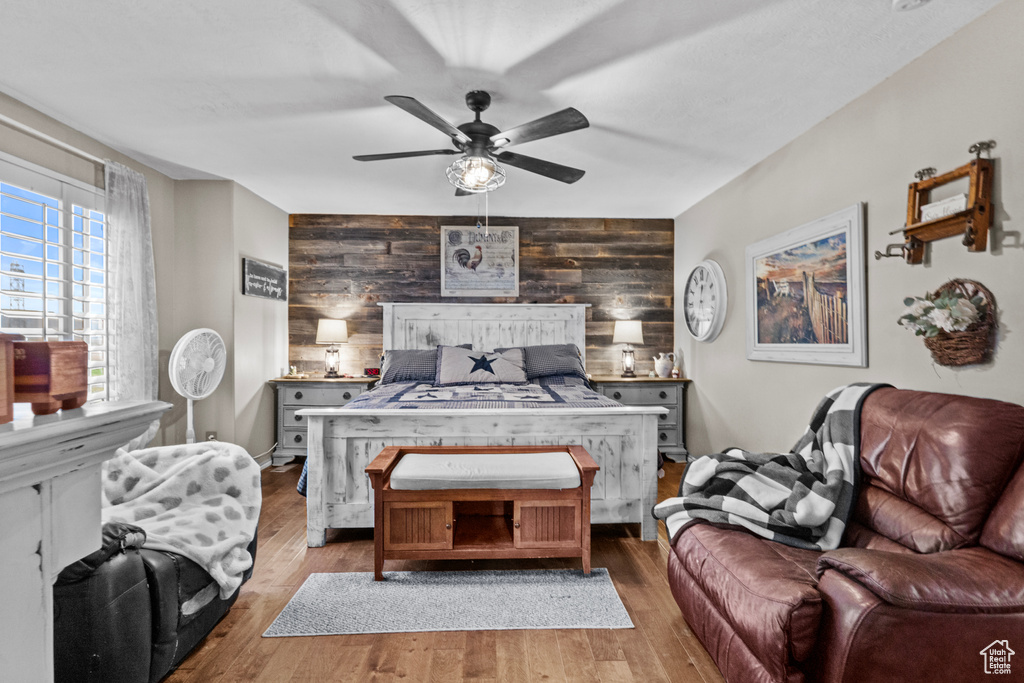 Bedroom featuring a ceiling fan, wood finished floors, an accent wall, and wooden walls
