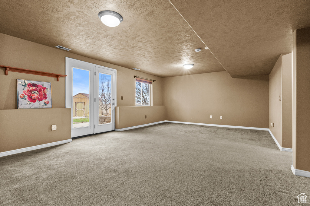 Carpeted empty room with baseboards, visible vents, and a textured ceiling