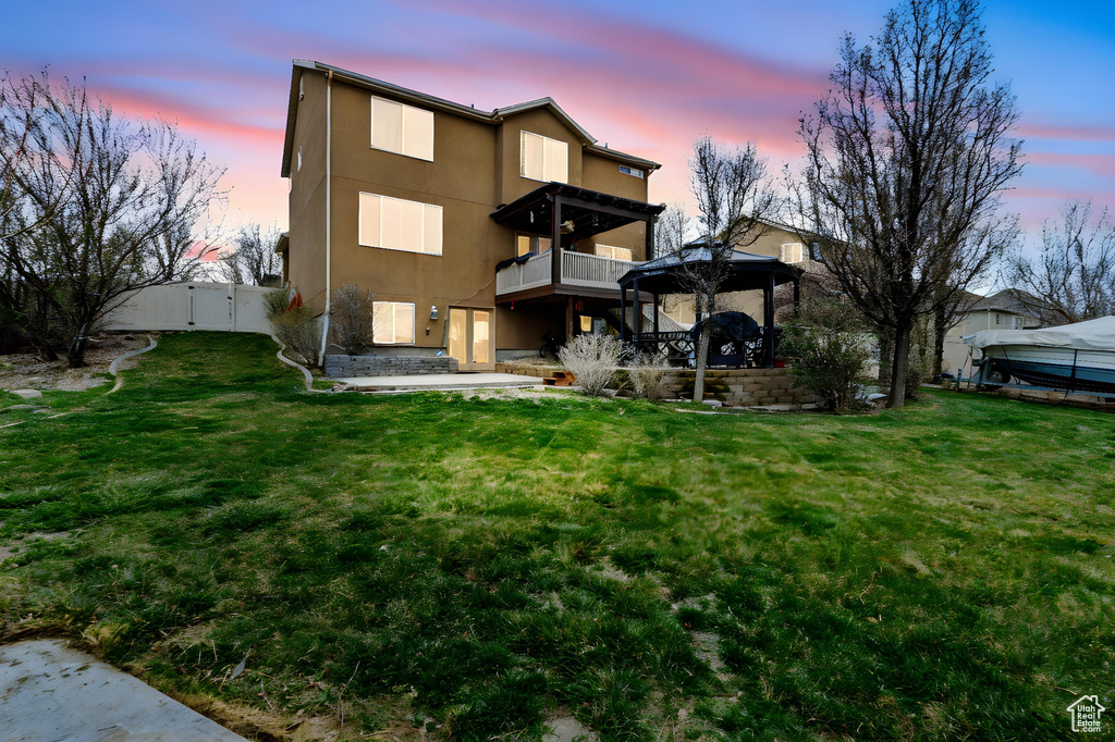 Back of house at dusk with stucco siding, a gazebo, a yard, and a patio area