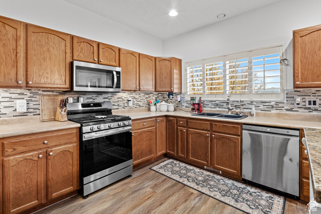 Kitchen featuring light countertops, backsplash, a sink, light wood-style floors, and appliances with stainless steel finishes