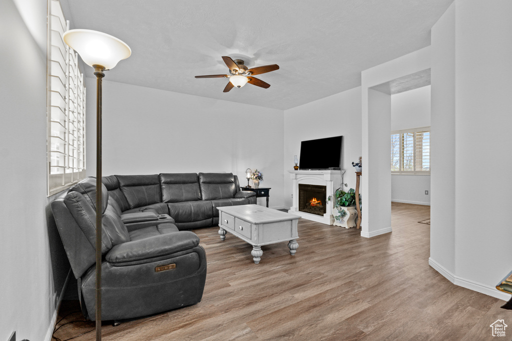 Living area featuring a warm lit fireplace, baseboards, wood finished floors, and a ceiling fan
