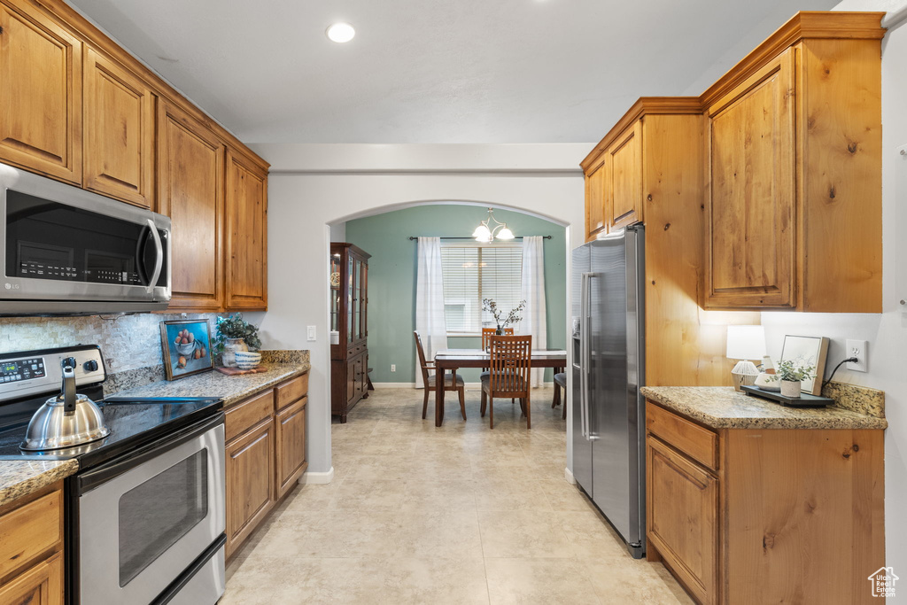 Kitchen with brown cabinets, an inviting chandelier, arched walkways, and stainless steel appliances
