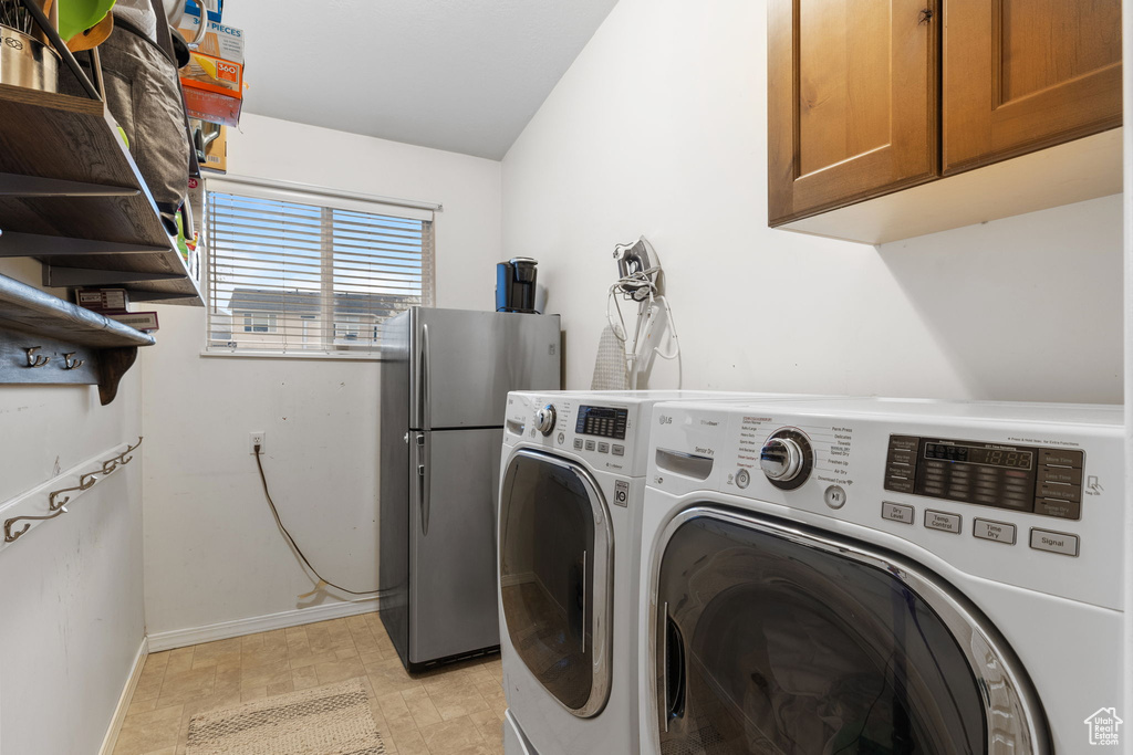Clothes washing area featuring washer and clothes dryer, cabinet space, and baseboards