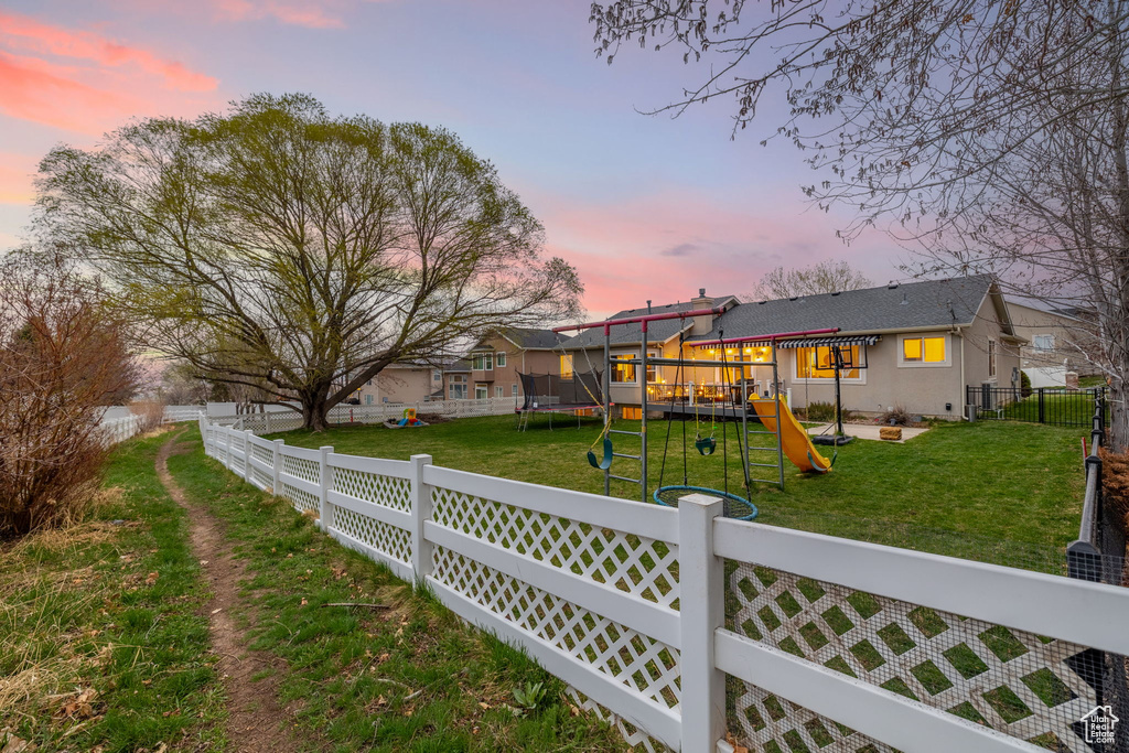 Back of property featuring a lawn, a trampoline, a playground, and a fenced backyard