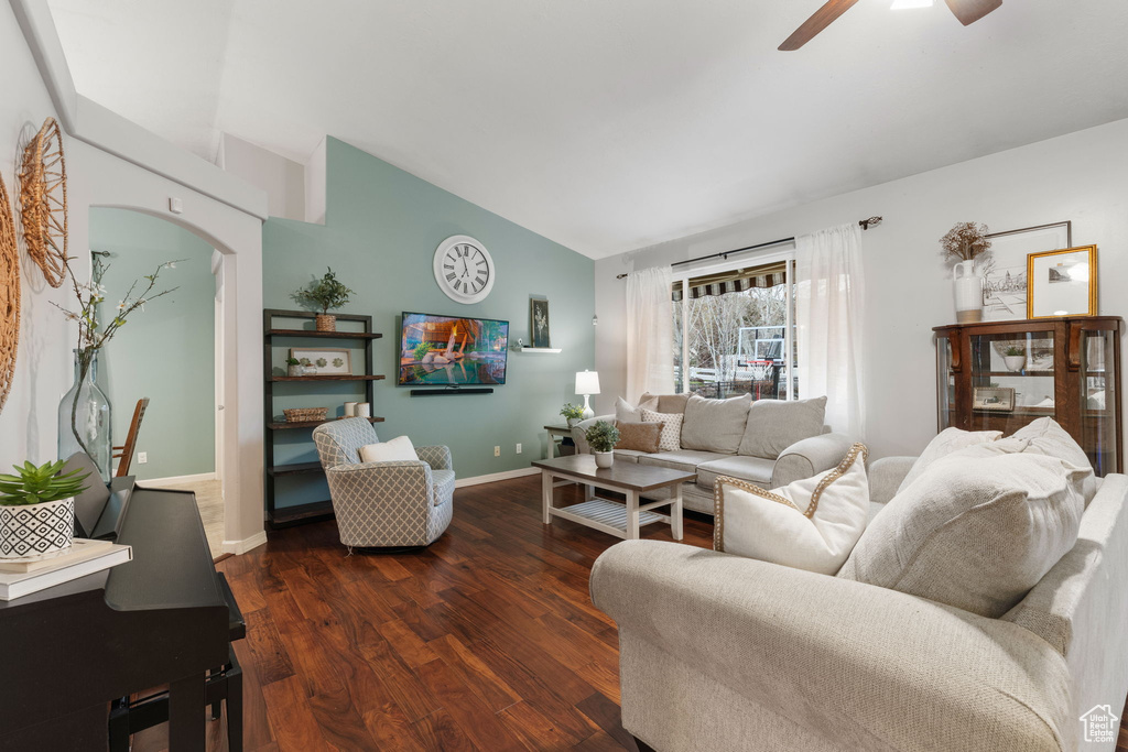 Living area featuring vaulted ceiling, dark wood-type flooring, baseboards, arched walkways, and a ceiling fan