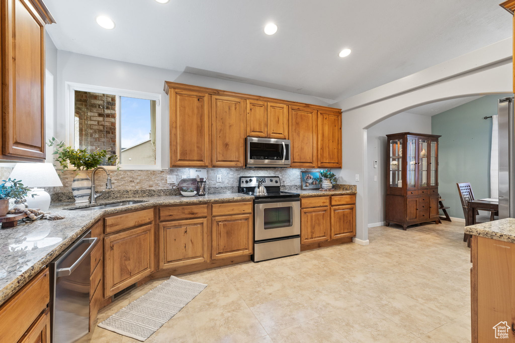 Kitchen with decorative backsplash, stainless steel appliances, arched walkways, a sink, and brown cabinetry