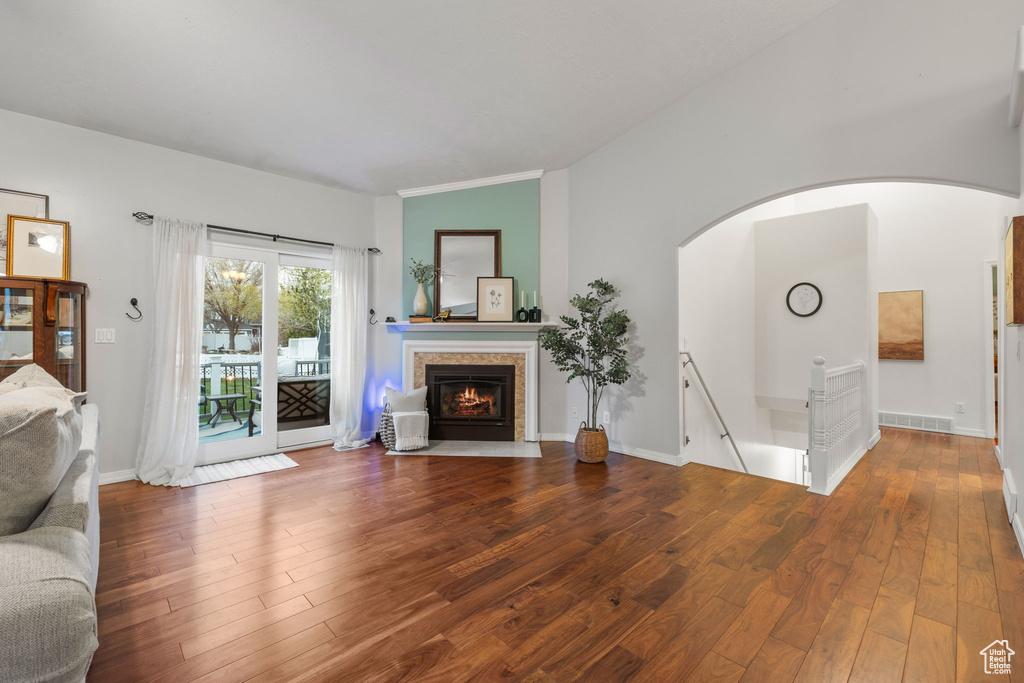 Unfurnished living room with lofted ceiling, arched walkways, a tile fireplace, and hardwood / wood-style floors