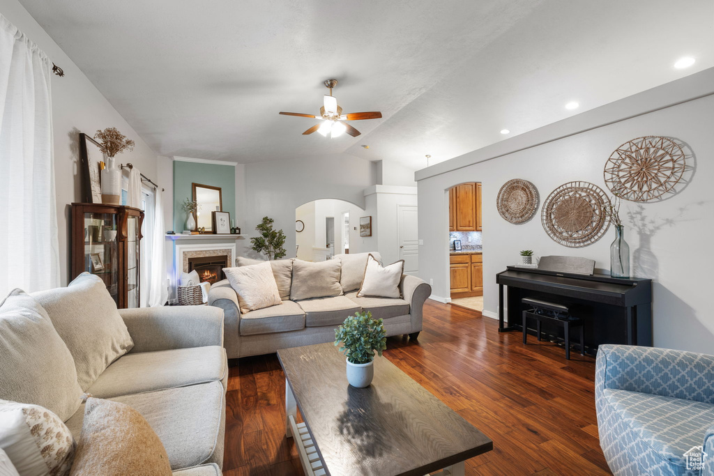 Living area featuring lofted ceiling, a ceiling fan, arched walkways, and dark wood-style flooring