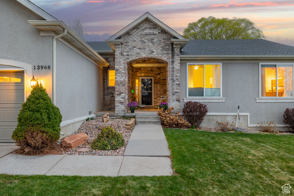 View of front of property featuring stucco siding, a shingled roof, brick siding, and a yard