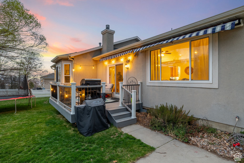 Exterior space with stucco siding, a lawn, a deck, a trampoline, and a chimney