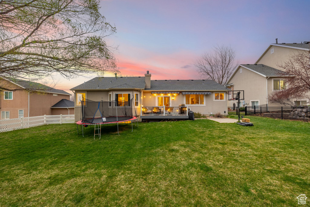 Back of property at dusk featuring a fenced backyard, a lawn, and a trampoline