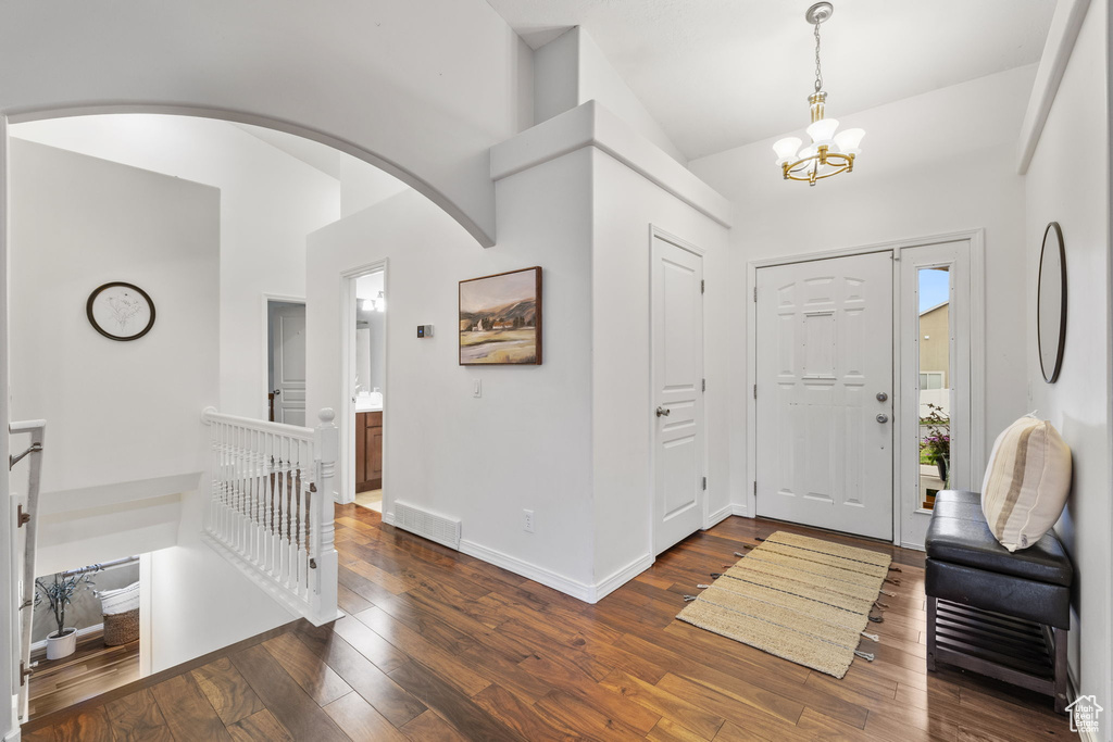 Entryway featuring visible vents, baseboards, arched walkways, dark wood-style floors, and an inviting chandelier