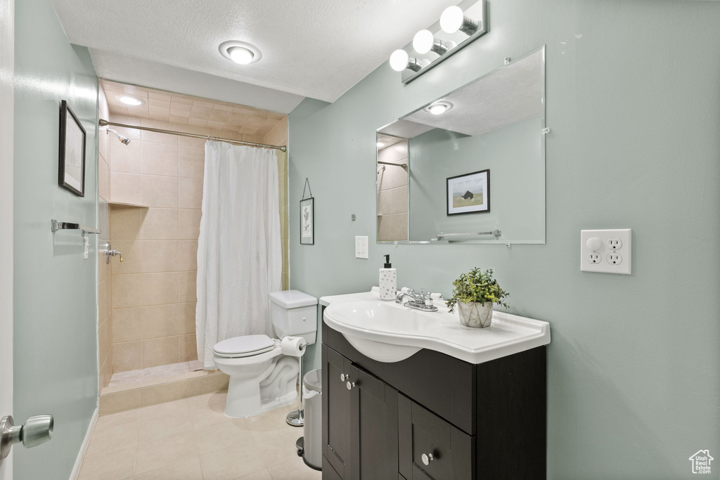 Bathroom with tile patterned floors, a tile shower, toilet, vanity, and baseboards