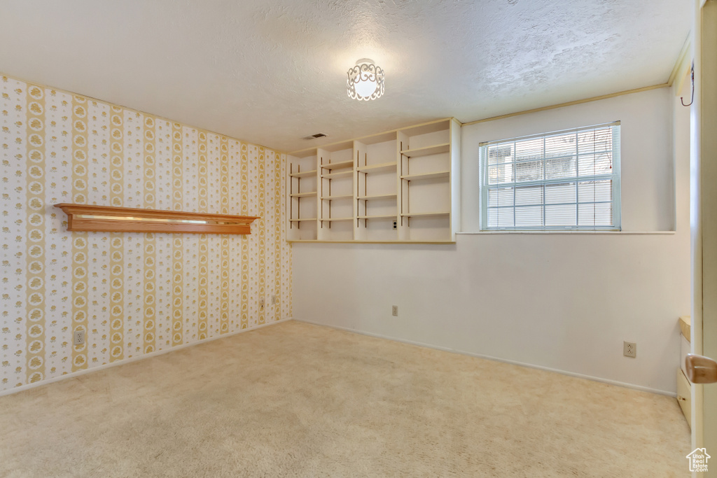 Carpeted spare room featuring baseboards, wallpapered walls, visible vents, and a textured ceiling