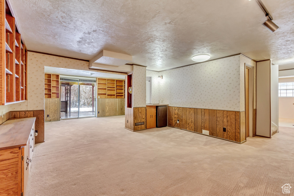 Below grade area featuring a wainscoted wall, a textured ceiling, wallpapered walls, and carpet