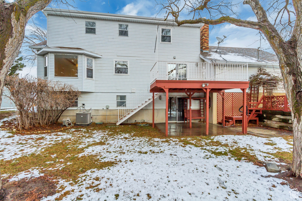 Snow covered house with stairs, cooling unit, and a wooden deck