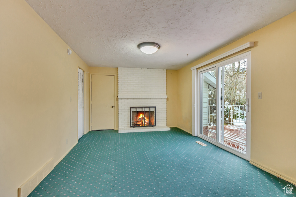 Unfurnished living room with a textured ceiling, visible vents, carpet, baseboards, and a fireplace