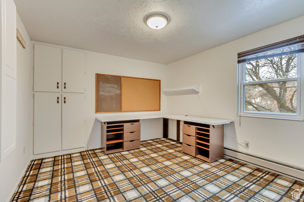 Unfurnished office featuring built in study area, a baseboard radiator, and a textured ceiling