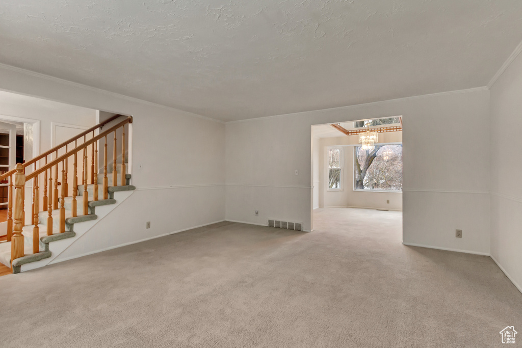 Unfurnished living room with carpet floors, stairway, visible vents, ornamental molding, and an inviting chandelier