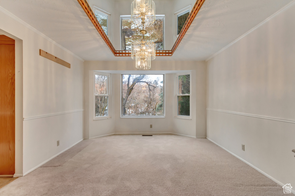 Carpeted empty room with ornamental molding, a notable chandelier, and baseboards