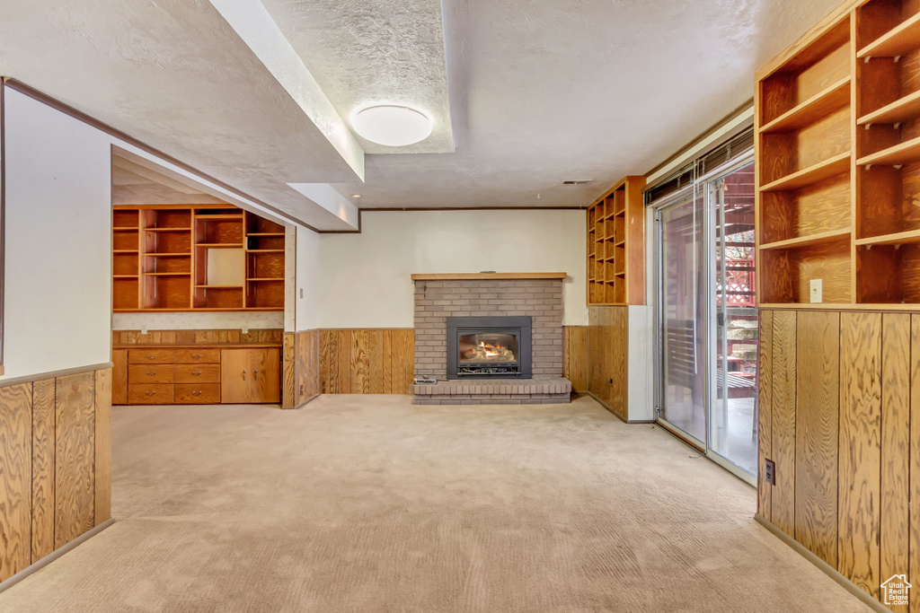 Unfurnished living room featuring carpet floors, wood walls, a brick fireplace, a textured ceiling, and wainscoting