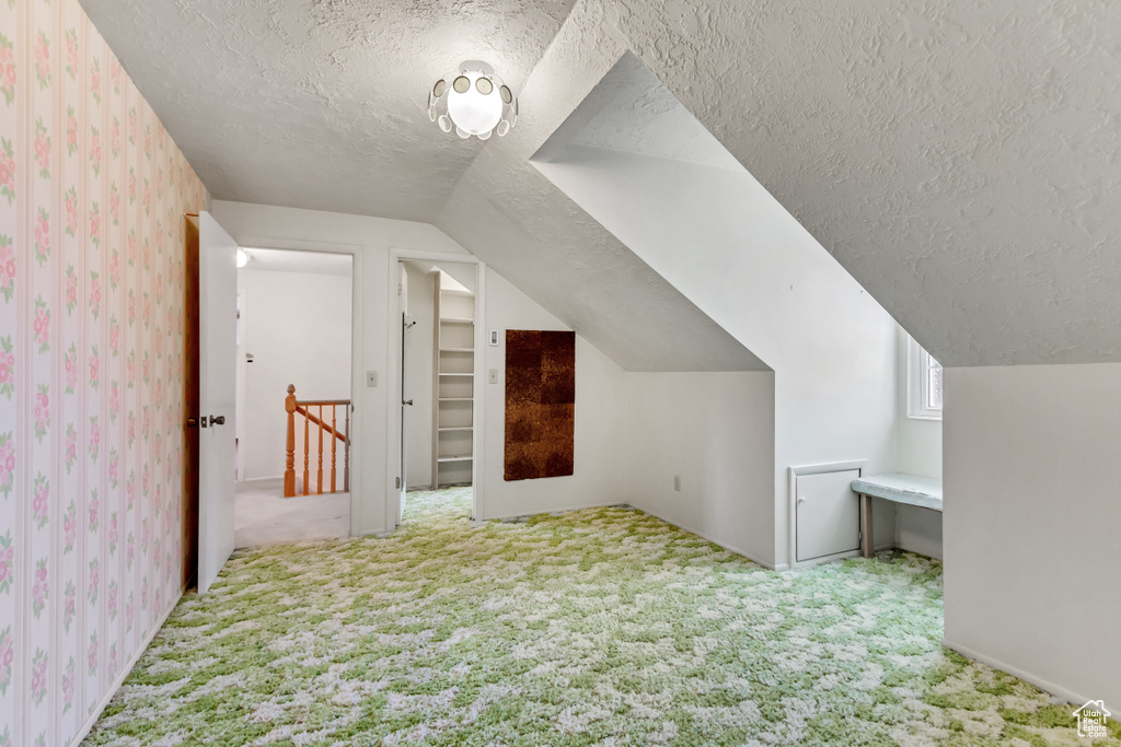 Additional living space with wallpapered walls, carpet floors, lofted ceiling, and a textured ceiling